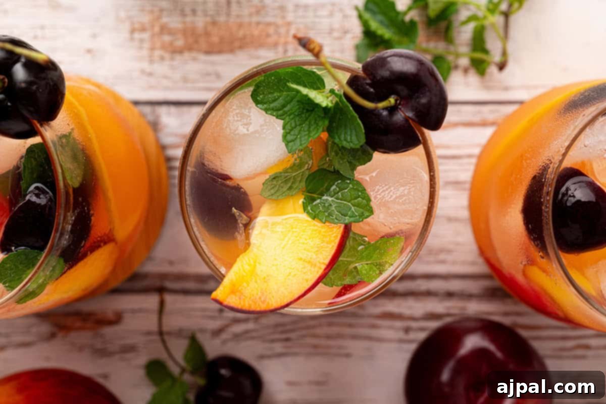 Vibrant Stone Fruit Refresher 11 Three glasses of refreshing stone fruit mocktail with peach slices, cherries, and mint leaves on a wooden surface, viewed from above.