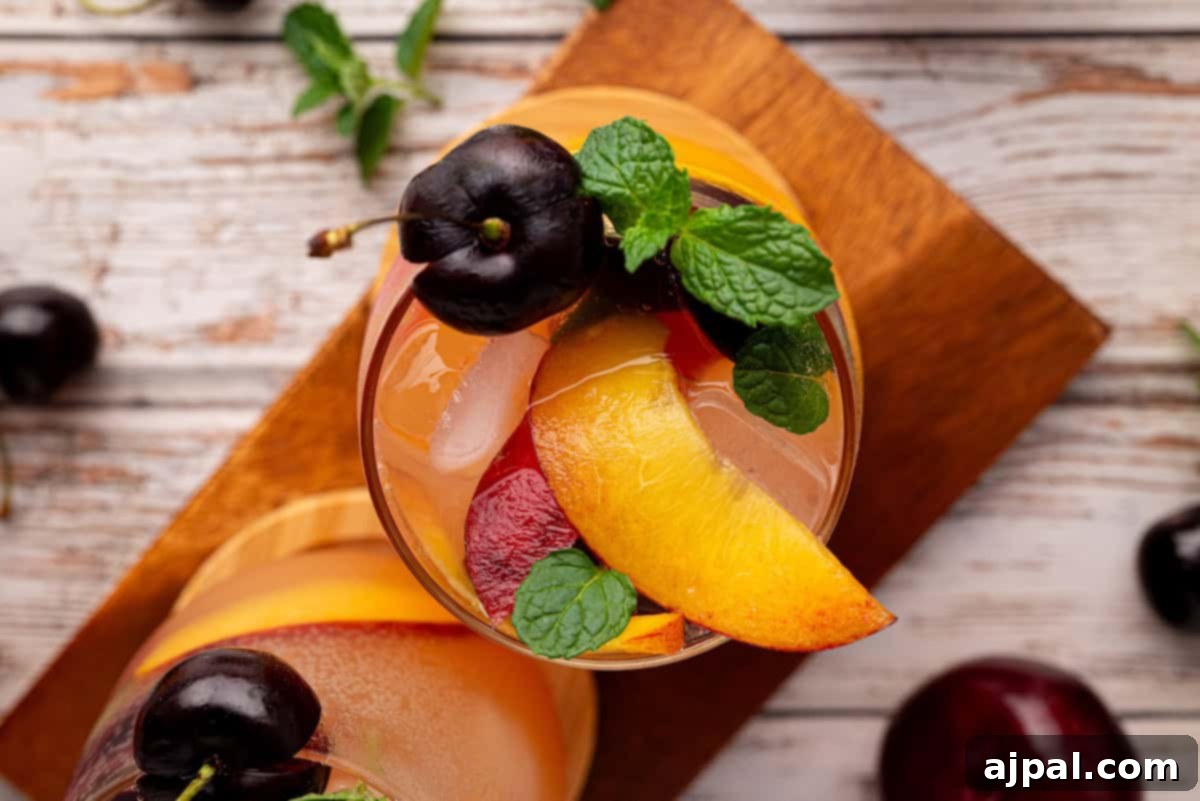 Vibrant Stone Fruit Refresher 13 A refreshing glass of stone fruit mocktail, garnished with peach slices, cherries, and fresh mint leaves, placed on a wooden board.