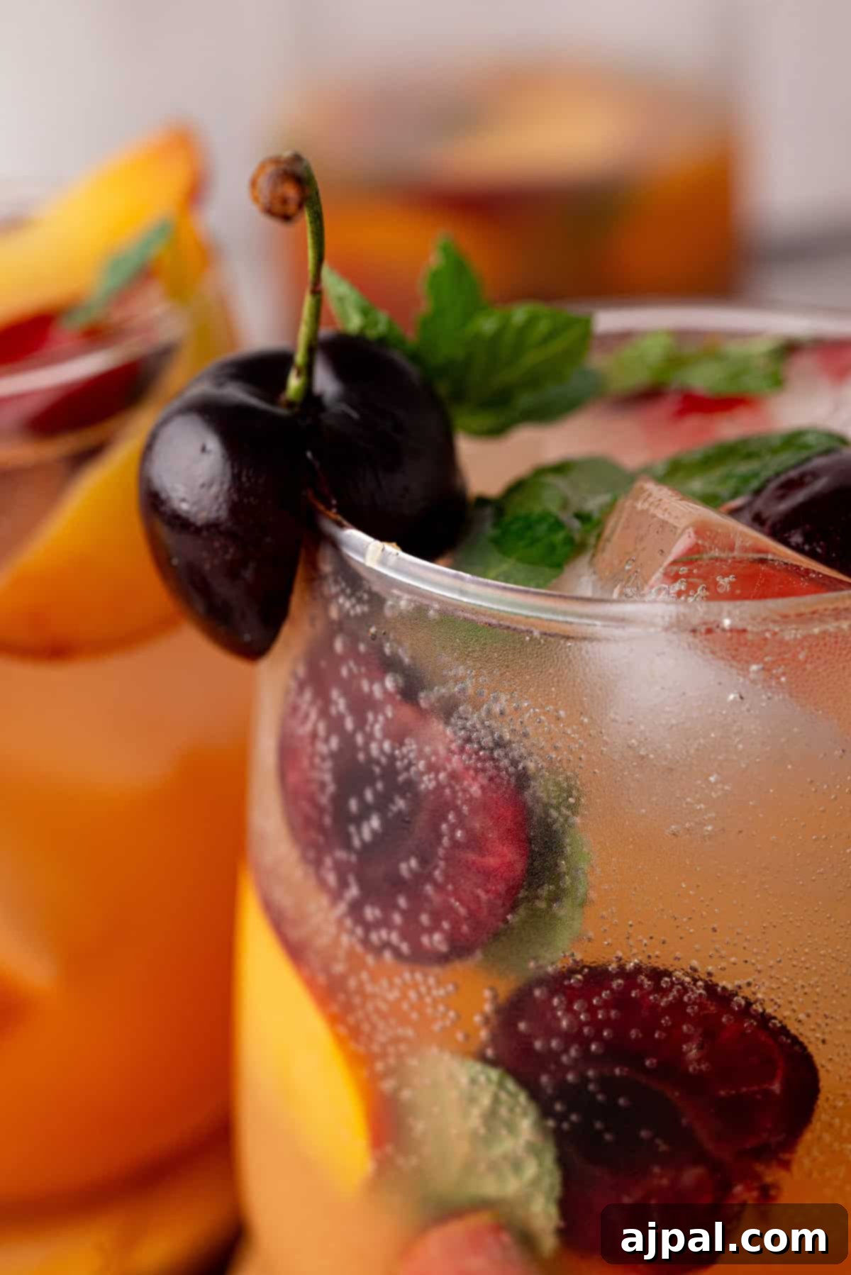 Vibrant Stone Fruit Refresher 3 Close-up of a glass filled with a sparkling Stone Fruit Sangria Mocktail, garnished with fresh cherries, peach slices, mint leaves, and ice cubes.
