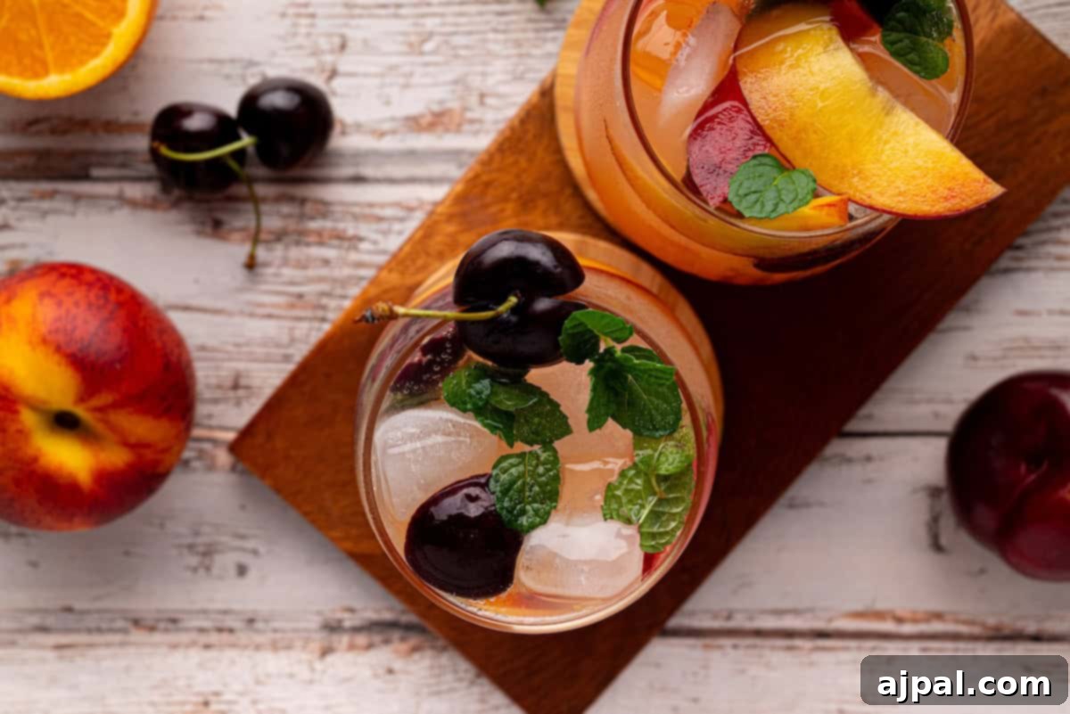 Vibrant Stone Fruit Refresher 10 Two glasses of refreshing stone fruit sangria mocktail garnished with cherries, mint leaves, and peach slices on a wooden board, with a nectarine, plum, and orange slice nearby.