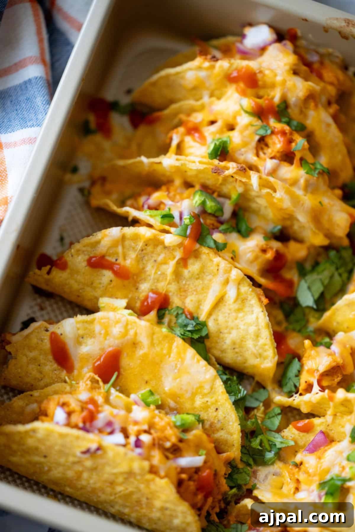 A baking tray of Baked Chicken Tacos filled with seasoned chicken, melted cheese, chopped onions, tomatoes, and fresh cilantro.