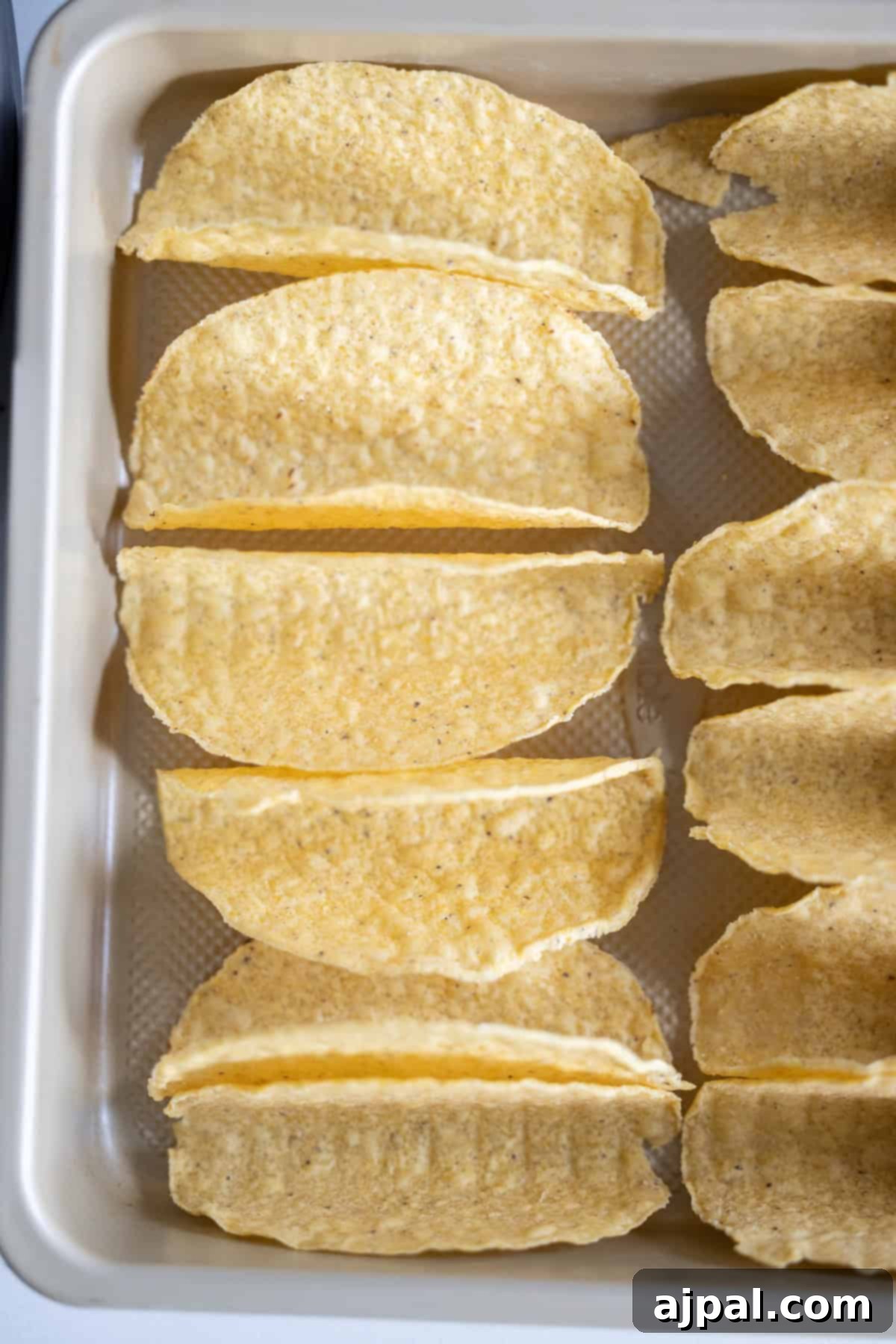 A baking tray lined with upright, empty hard taco shells arranged in rows, ready to be filled for delicious Baked Chicken Tacos.