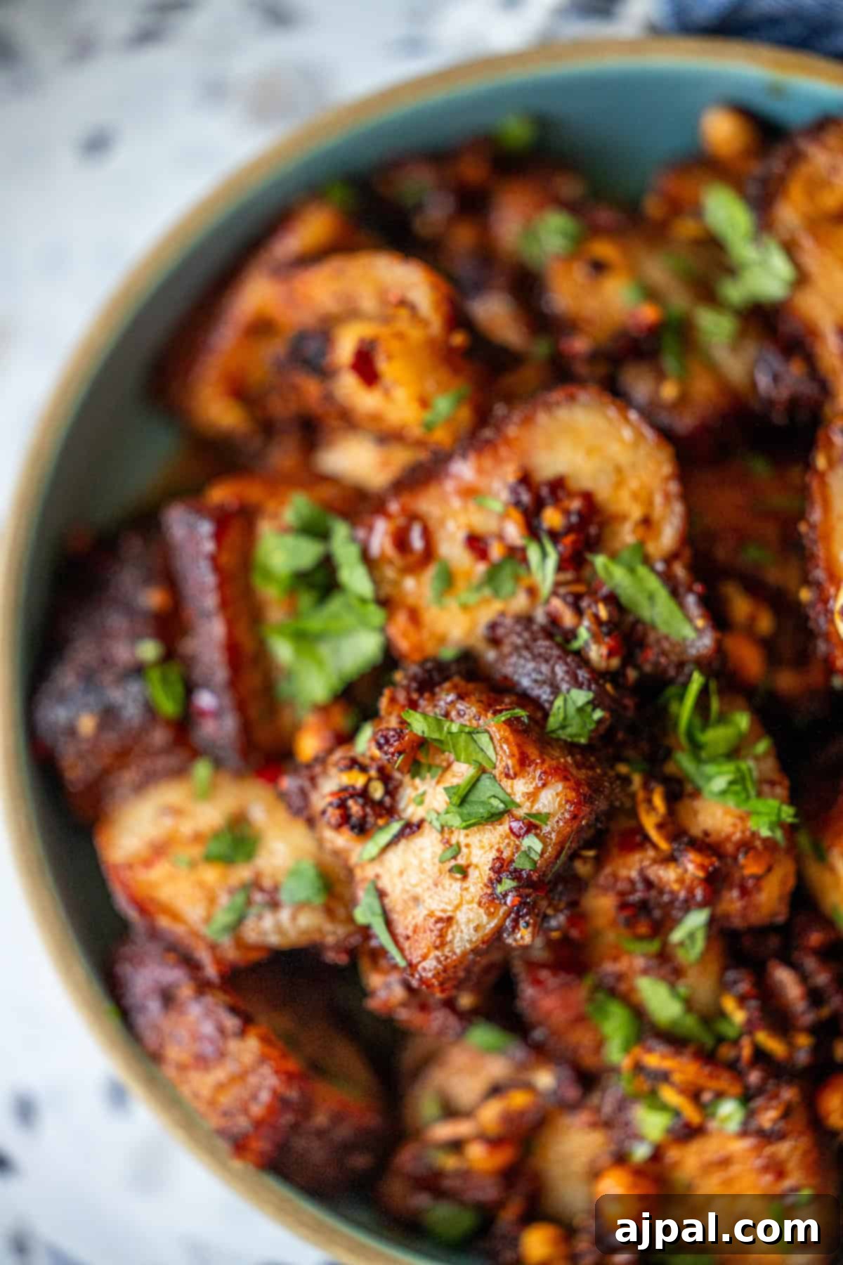 Glazed Asian Pork Belly Morsels 5 A bowl filled with roasted, seasoned potato cubes garnished with chopped fresh herbs, perfect as a side dish to Sticky Asian Pork Belly.