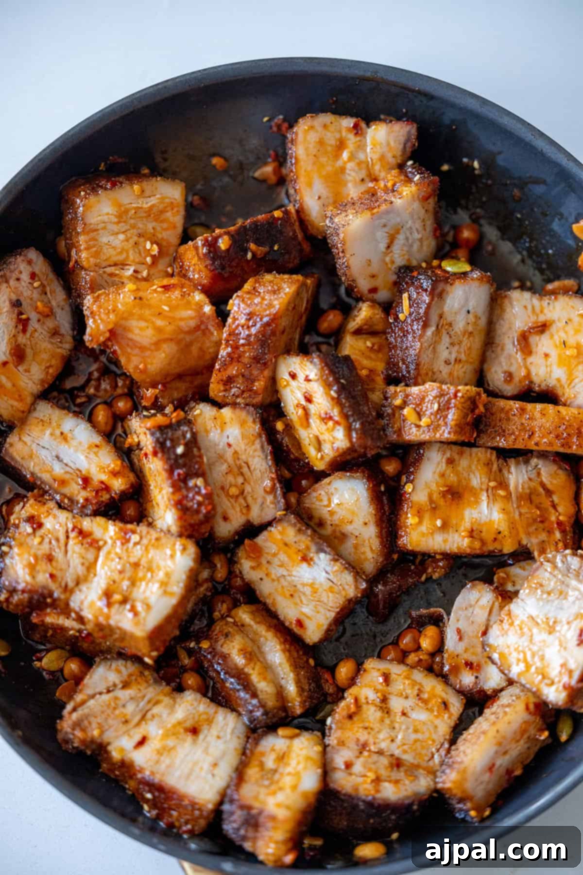 Glazed Asian Pork Belly Morsels 8 Pan of cooked, cubed Sticky Asian Pork Belly pieces with a spicy seasoning and some peanuts, showing a crispy texture and golden-brown color.