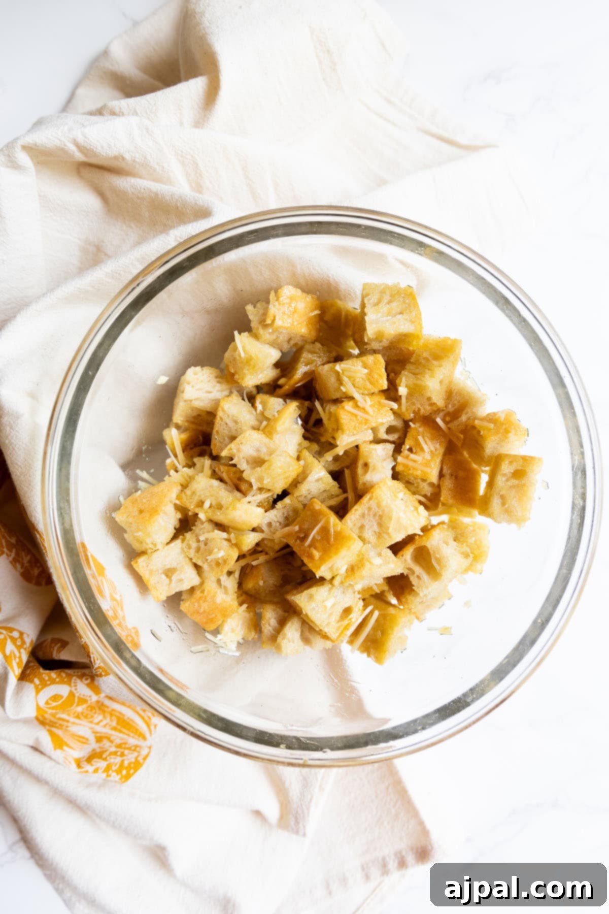 Crunchy Bread Bites 6 A glass bowl filled with homemade croutons and shredded cheese, set on a white cloth.