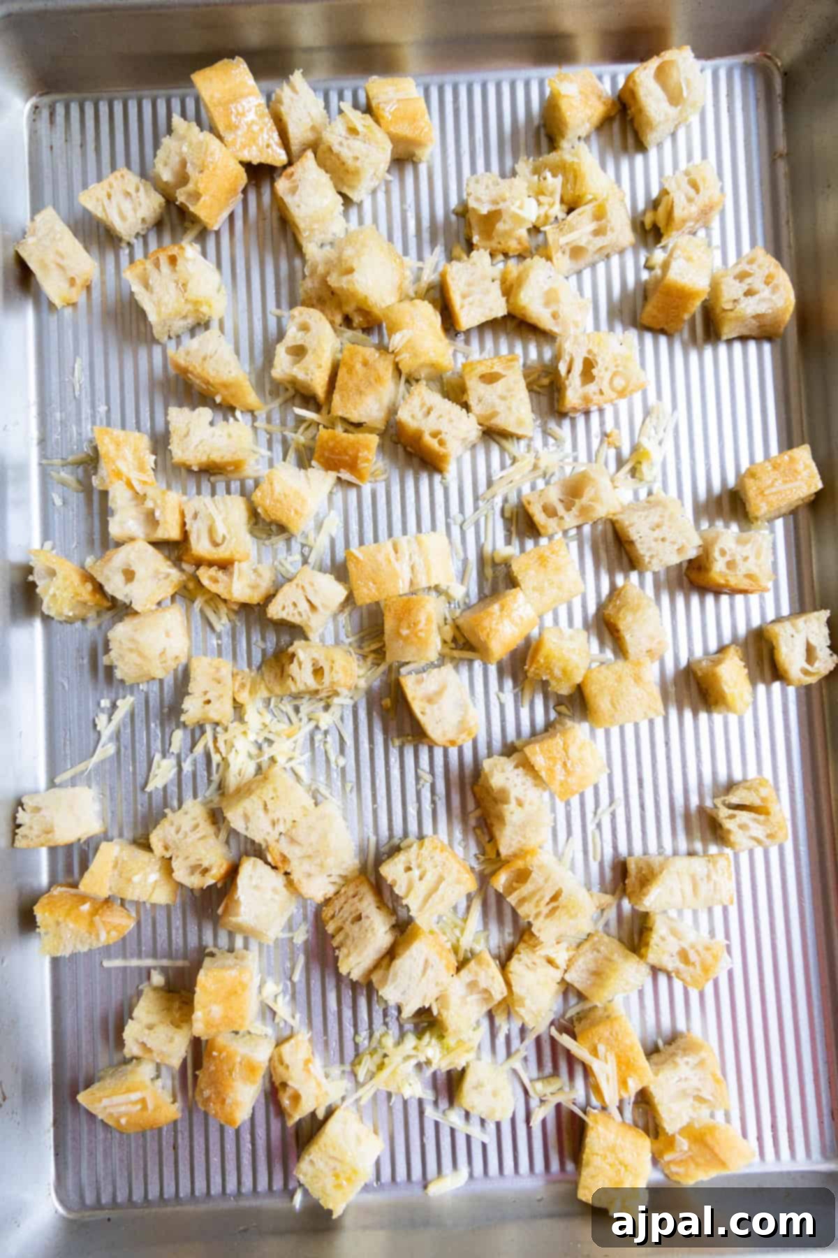 Crunchy Bread Bites 7 Cubes of bread and shredded cheese, soon to become homemade croutons, are scattered on a metal baking tray.