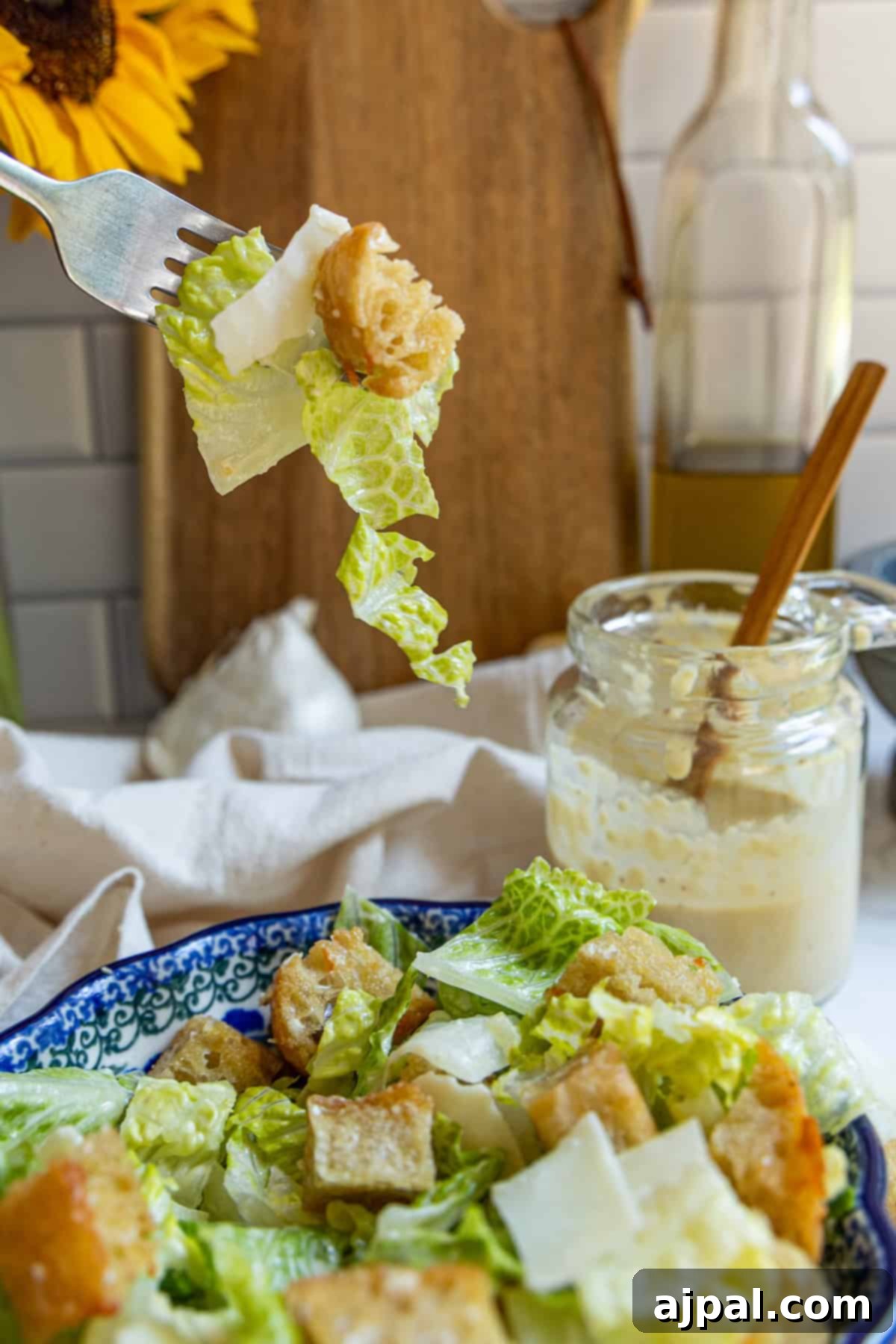 The Ultimate Caesar Salad 3 A fork holding a perfect bite of Caesar salad, showcasing fresh lettuce, a crunchy crouton, and a piece of Parmesan. In the background, a jar of homemade Caesar dressing and olive oil hint at the fresh ingredients.