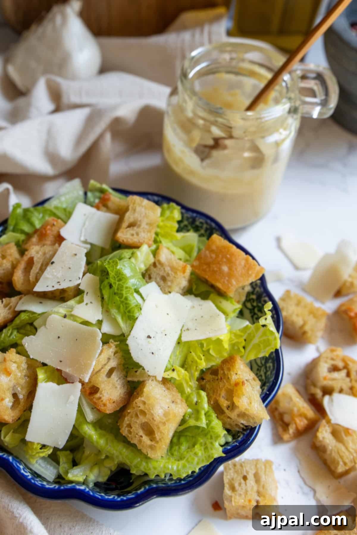 The Ultimate Caesar Salad 4 A beautifully presented bowl of Caesar salad, featuring vibrant romaine lettuce, golden-brown croutons, and delicate shaved cheese, alongside a jar of creamy homemade Caesar dressing with a spoon.
