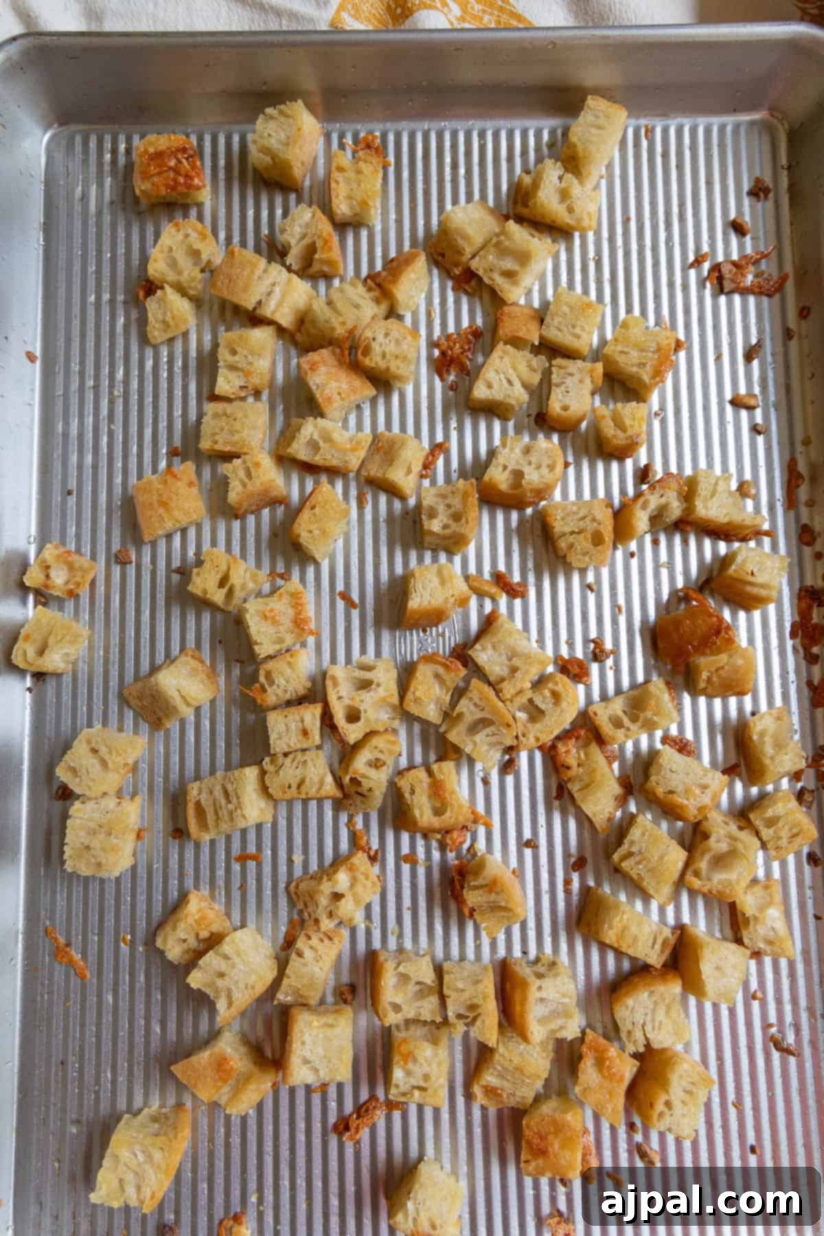 The Ultimate Caesar Salad 5 Cubed pieces of perfectly toasted bread are scattered on a ridged metal baking sheet, some with melted cheese and a hint of a golden, savory drizzle, ready to become the best homemade croutons.