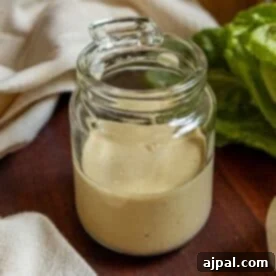A glass jar brimming with creamy homemade Caesar dressing, accompanied by a wooden spoon and a fresh lettuce leaf on a rustic wooden surface, perfectly capturing the essence of fresh, delicious condiment.
