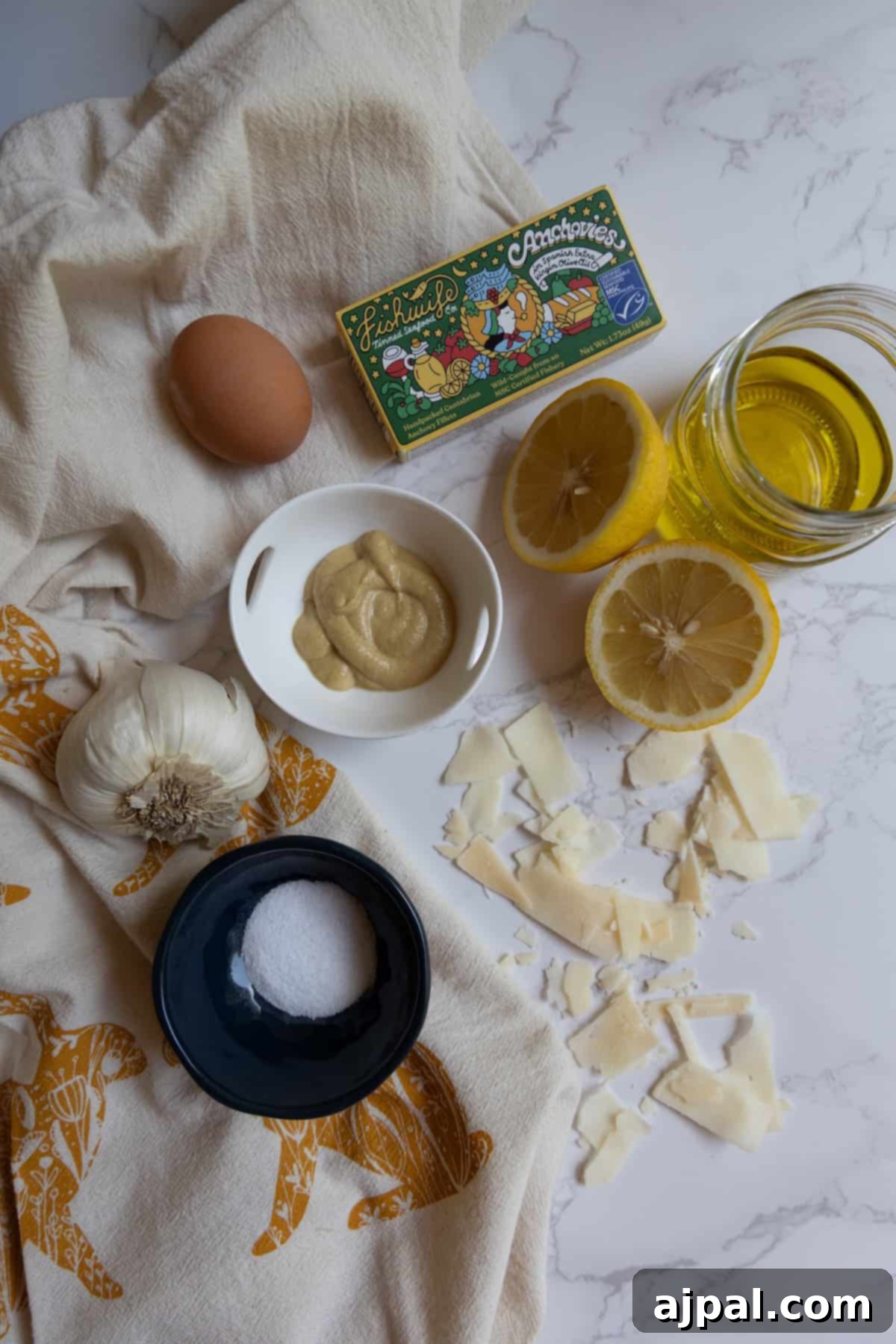Ingredients for a homemade Caesar dressing recipe neatly arranged on a pristine white surface: a whole egg, a dollop of Dijon mustard, vibrant lemon halves, golden olive oil, fresh garlic cloves, fine sea salt, delicate shavings of Parmesan cheese, and a small box of oil-packed anchovies, showcasing the freshness and quality of each component.