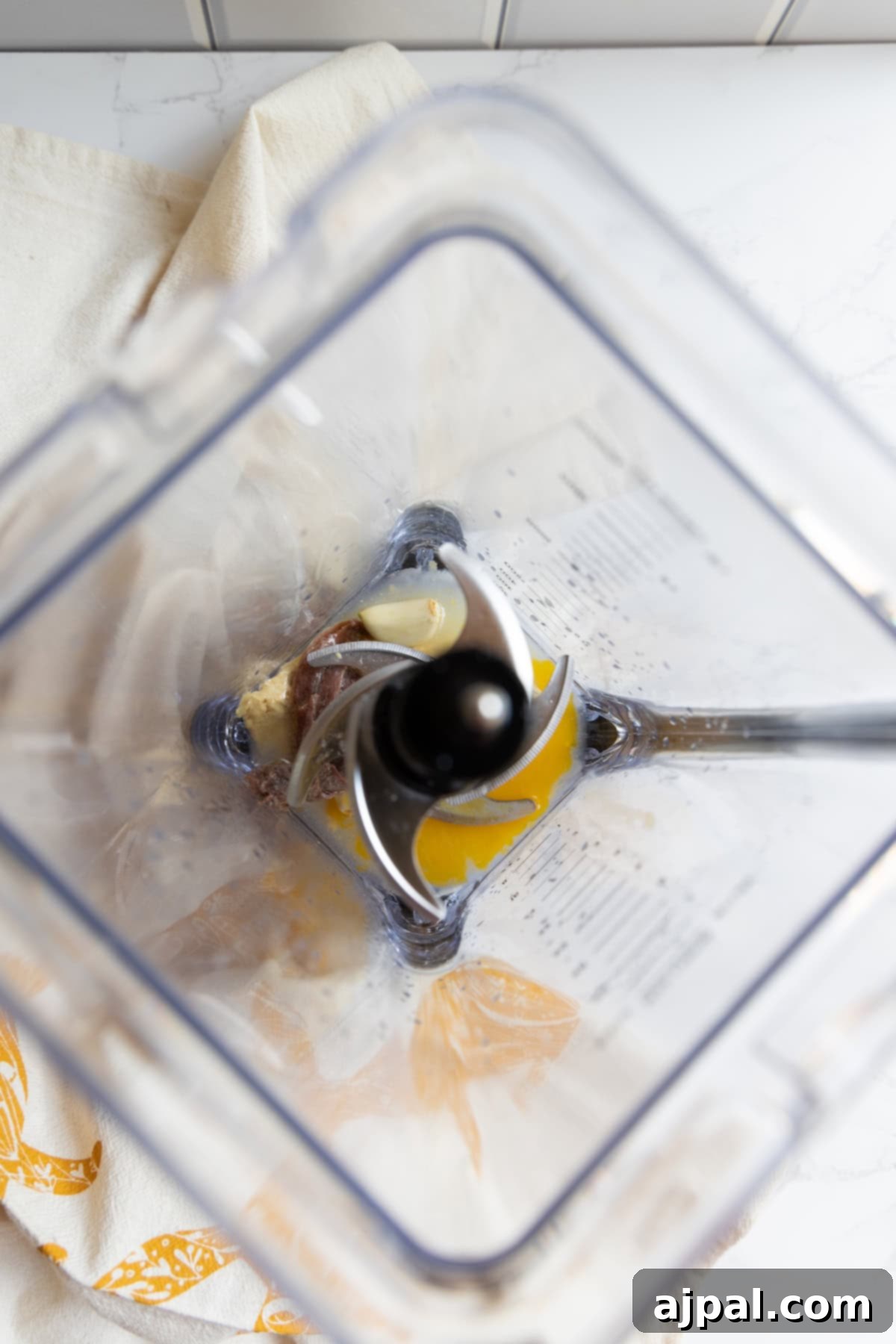 Top view of an empty blender with streaks of caesar dressing residue left on the sides, sitting on a white counter with a beige and orange towel underneath.
