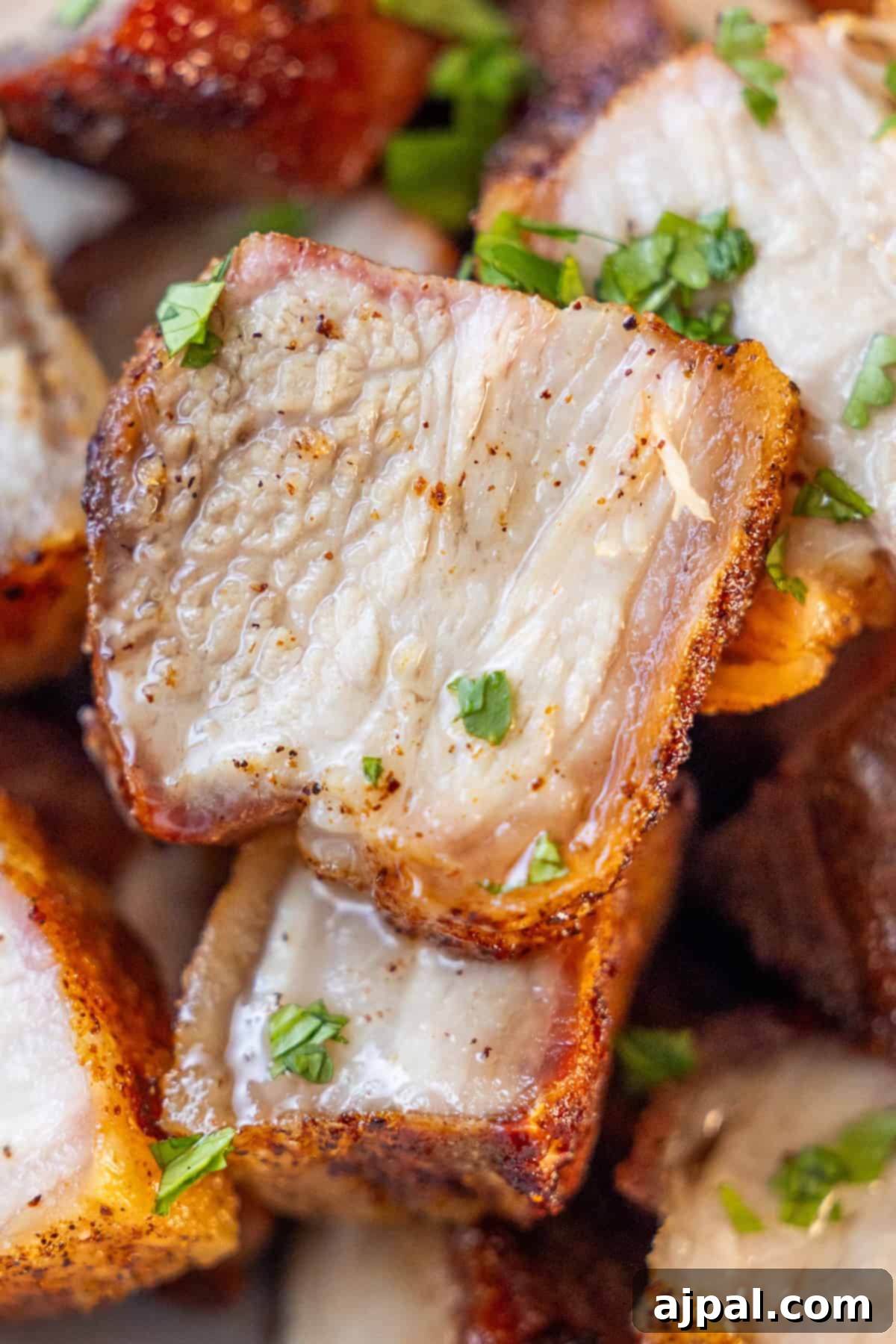 Ultimate Crispy Pork Belly 2 Close-up of crispy, roasted pork belly pieces, perfectly seasoned and garnished with chopped fresh herbs.