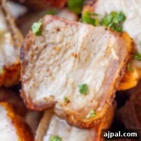 Close-up of crispy, roasted pork belly slices garnished with chopped fresh herbs.