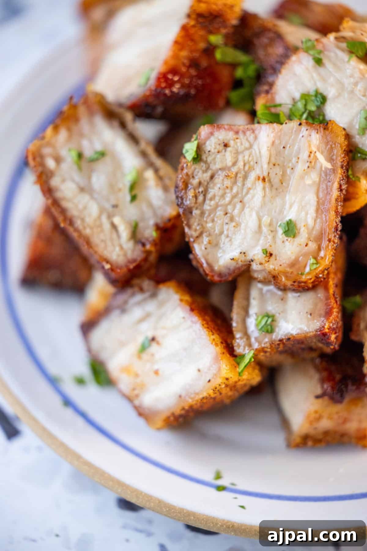 Ultimate Crispy Pork Belly 5 A plate filled with several pieces of crispy, roasted pork belly garnished with chopped herbs.