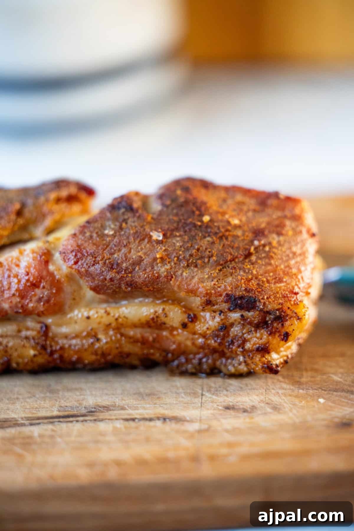 Ultimate Crispy Pork Belly 8 A close-up of roasted pork belly resting on a wooden cutting board, showcasing its seasoned, crispy surface.