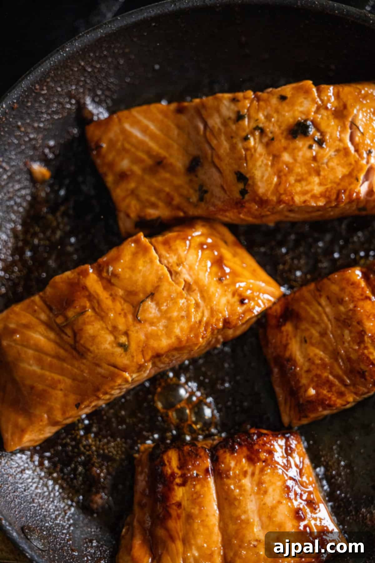 Four pieces of Japanese BBQ Salmon fillets cook to perfection in a black skillet, their glazed surfaces sizzling irresistibly.