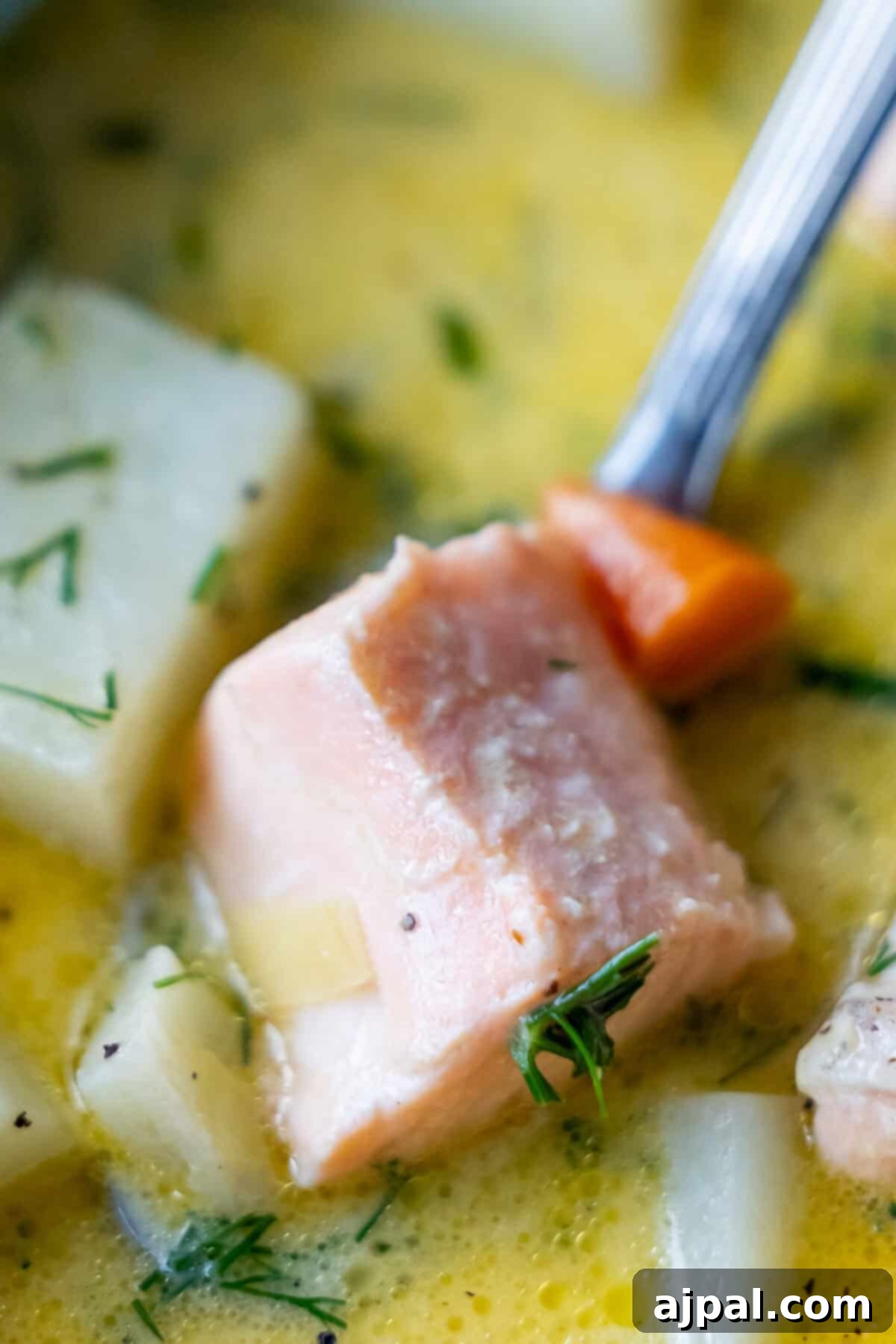 Traditional Finnish Salmon Soup 2 Close-up of a spoonful of creamy Finnish Salmon Chowder (lohikeitto) featuring salmon, diced potato, carrot, and fresh herbs in a vibrant yellow broth.