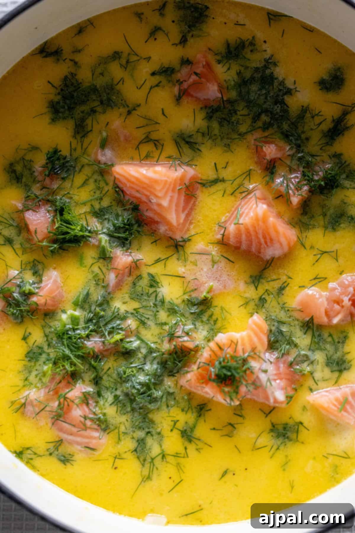 Traditional Finnish Salmon Soup 11 Chunks of raw salmon and fresh dill in a yellow, creamy soup base inside a pot—classic Finnish Salmon Chowder, also known as lohikeitto.