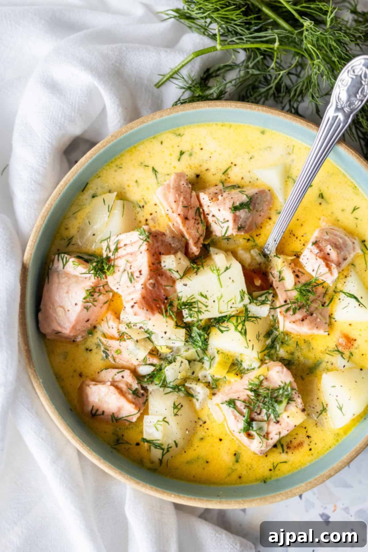 Traditional Finnish Salmon Soup 12 A bowl of creamy Finnish Salmon Chowder (lohikeitto) with chunks of salmon, potatoes, and herbs, garnished with fresh dill, and a spoon resting in the bowl.