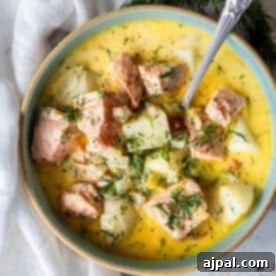 Traditional Finnish Salmon Soup 13 A bowl of creamy Finnish Salmon Chowder (lohikeitto) with chunks of salmon, potatoes, fresh dill, and a spoon, set on a white surface with a napkin.