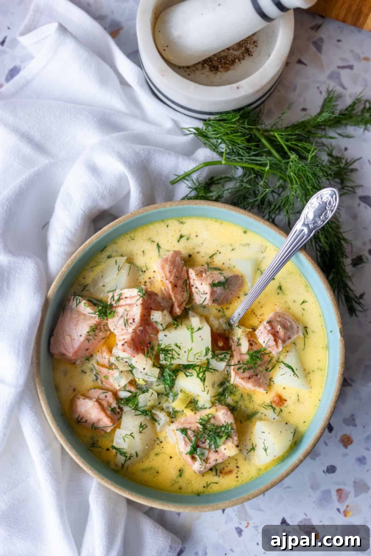Traditional Finnish Salmon Soup 4 A bowl of creamy Finnish salmon chowder, or lohikeitto, with chunks of salmon, potatoes, and fresh dill sits next to a white napkin, mortar and pestle, and sprigs of dill.