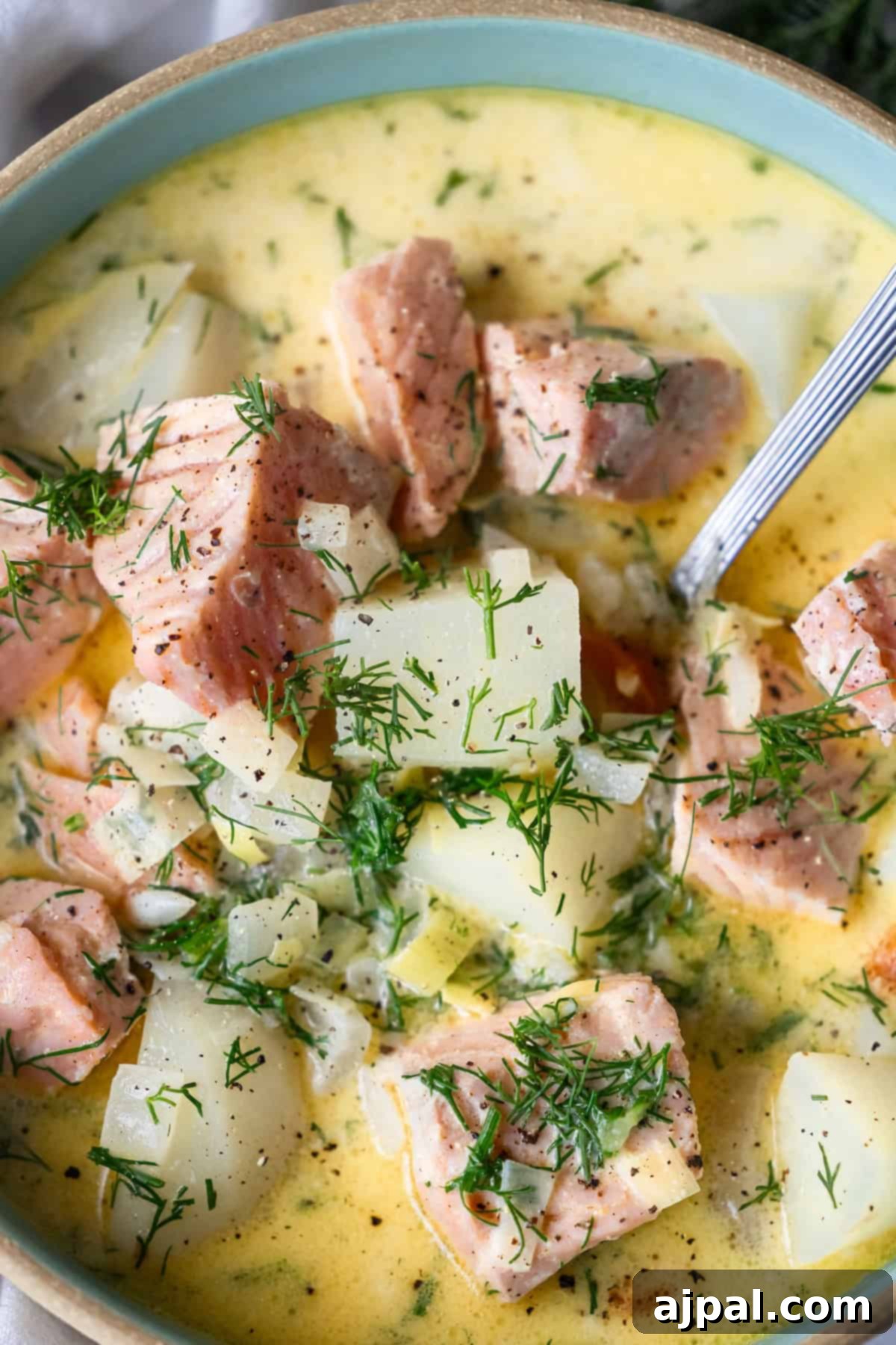Traditional Finnish Salmon Soup 5 A bowl of creamy Finnish Salmon Chowder, or lohikeitto, with chunks of salmon, potatoes, onions, and fresh dill, with a spoon partially visible.