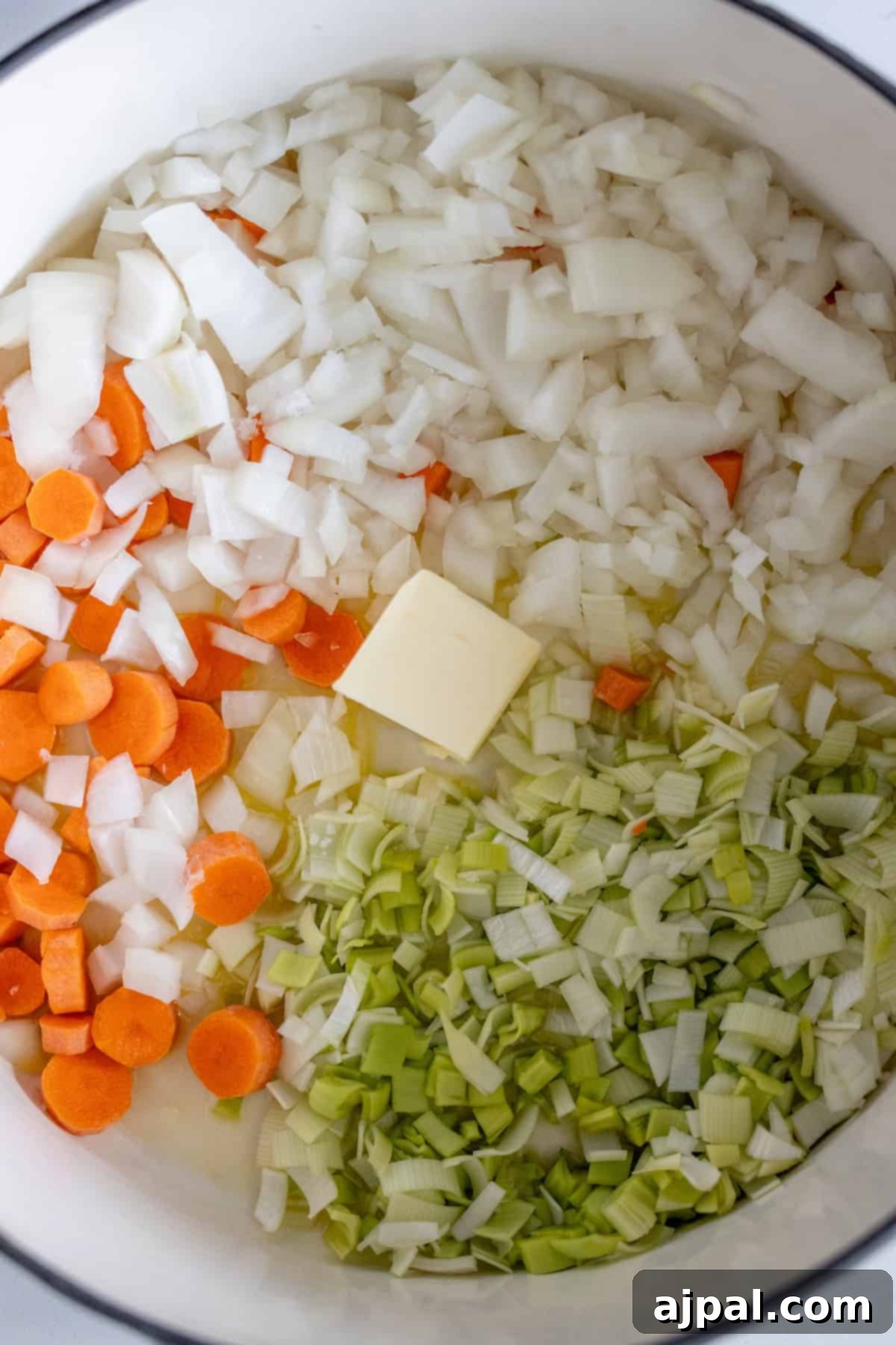 Traditional Finnish Salmon Soup 6 Chopped onions, carrots, and leeks with a pat of butter in a white pot, ready to be cooked for a delicious Finnish Salmon Chowder.
