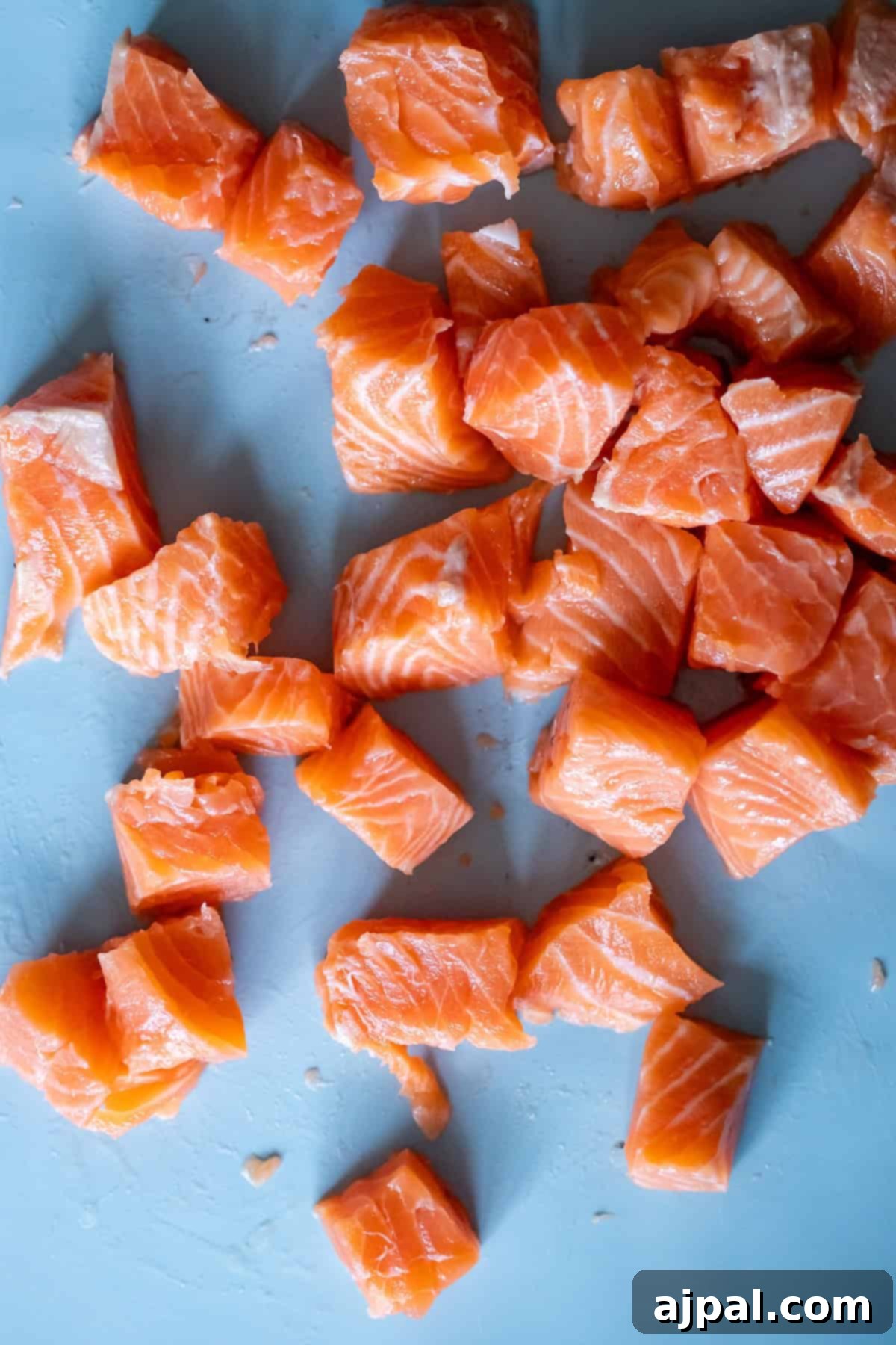 Traditional Finnish Salmon Soup 7 Cubes of raw salmon, perfect for crafting lohikeitto or Finnish Salmon Chowder, are scattered on a light blue surface.