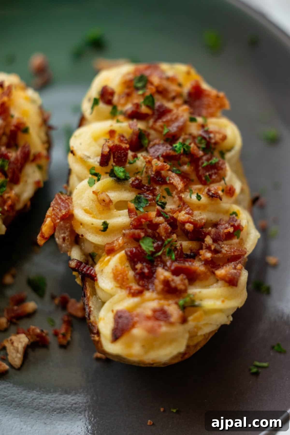 The Ultimate Double-Baked Potato 5 A beautifully piped twice-baked potato half, generously topped with golden-brown crispy bacon bits and finely chopped parsley, presented on a dark plate.