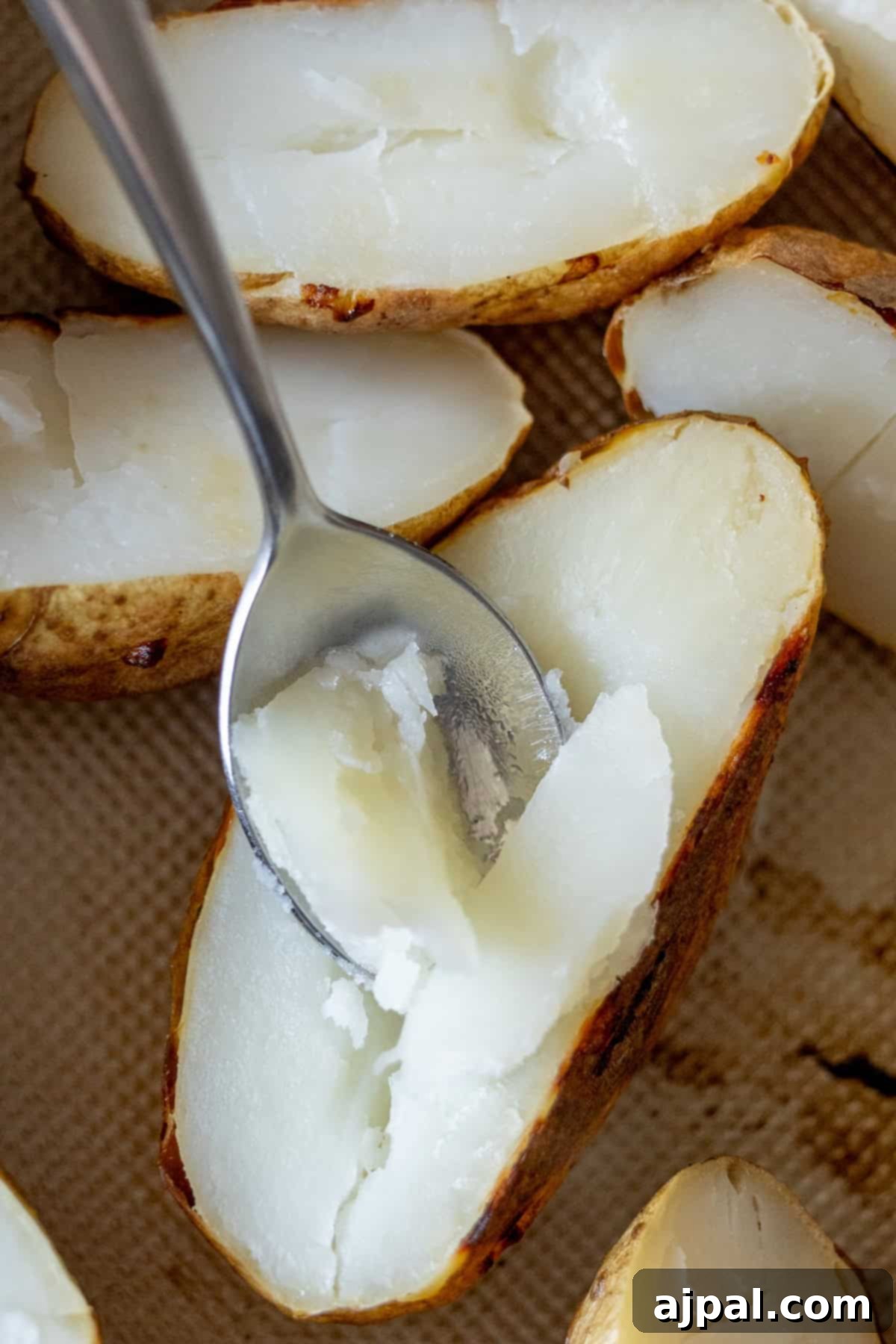 The Ultimate Double-Baked Potato 7 A spoon gently scoops out the fluffy interior of a perfectly baked potato half, prepared for the creamy filling of a twice-baked potato recipe.