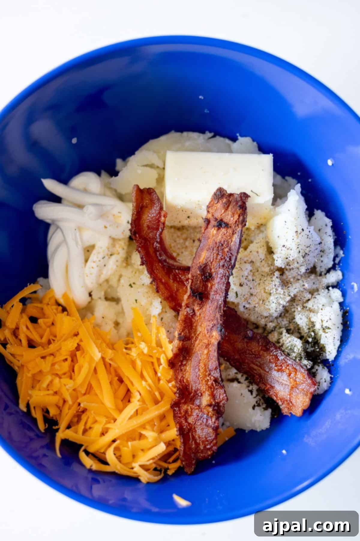 The Ultimate Double-Baked Potato 8 A blue bowl filled with rich mashed potato pulp, ready to be transformed into a creamy filling for twice-baked potatoes, showcasing key ingredients like bacon, cheese, and butter.