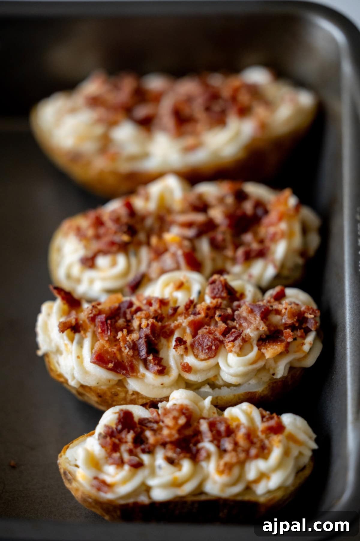 The Ultimate Double-Baked Potato 9 Four beautifully prepared loaded potato halves, meticulously piped with fluffy mashed potatoes and generously topped with crispy crumbled bacon, arranged in a baking pan, ready for the final bake.