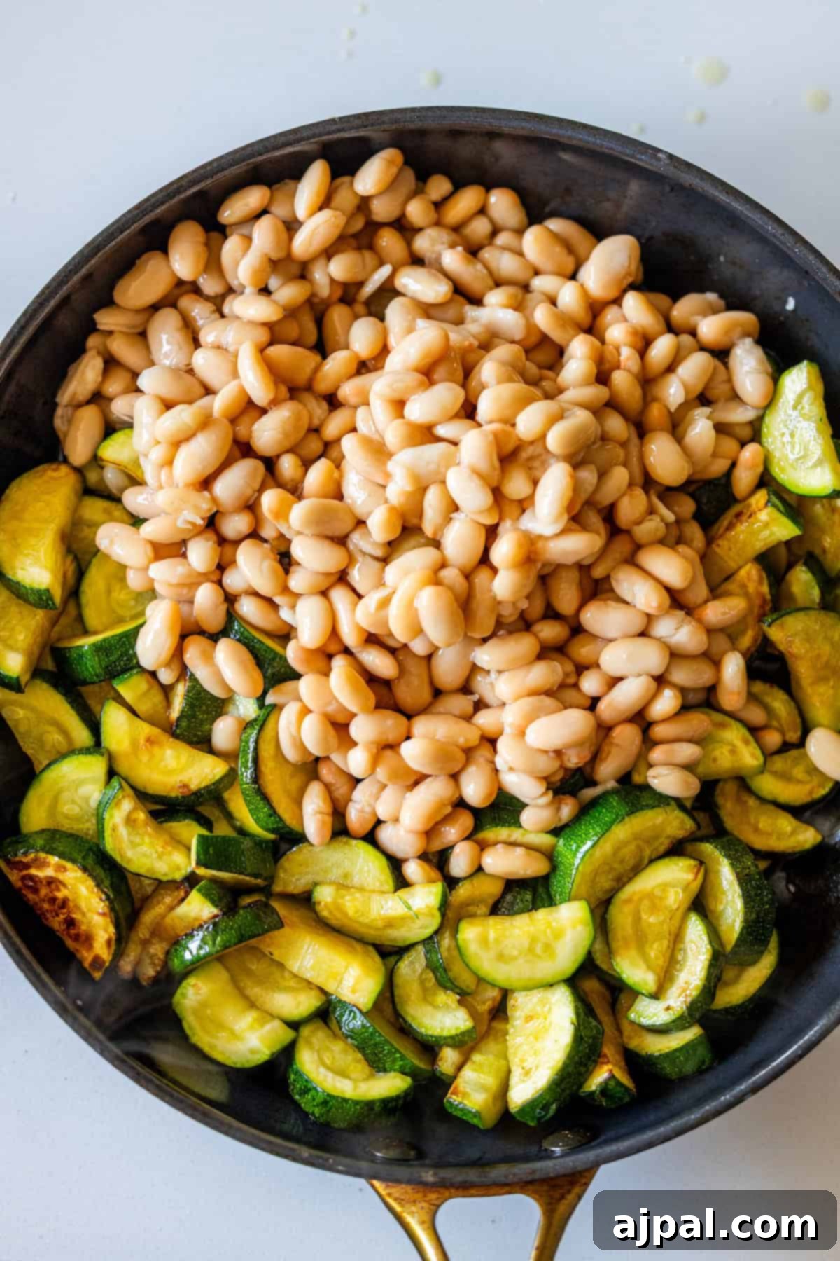 Marry Me Zucchini and Bean Delight 11 A skillet filled with cooked sliced zucchini and a pile of white beans on top, ready to be mixed together for a dish that will make you say "marry me" with every bite.