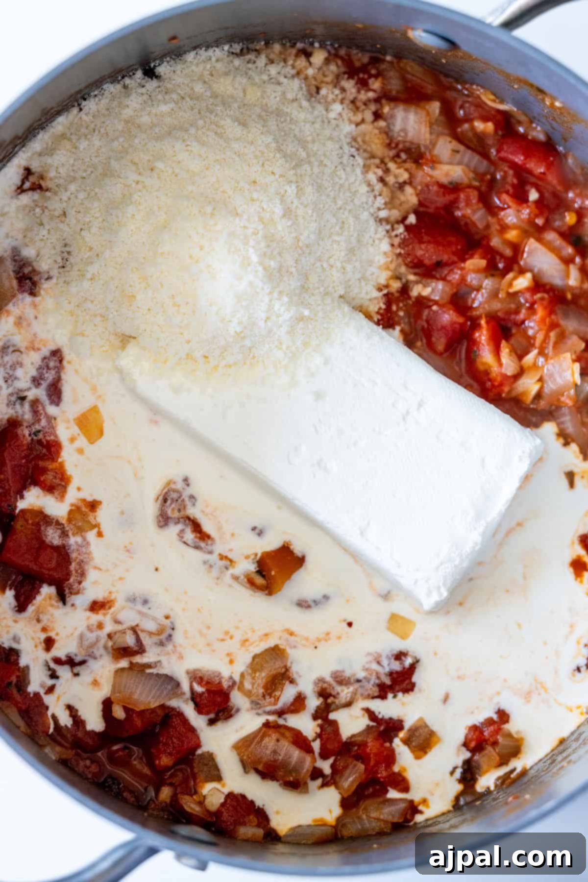 Marry Me Zucchini and Bean Delight 10 A pot containing cooked onions, diced tomatoes, a block of cream cheese, grated Parmesan cheese, cream, and zucchini—this Marry Me Zucchini is a creamy vegetarian recipe ready to be mixed together.