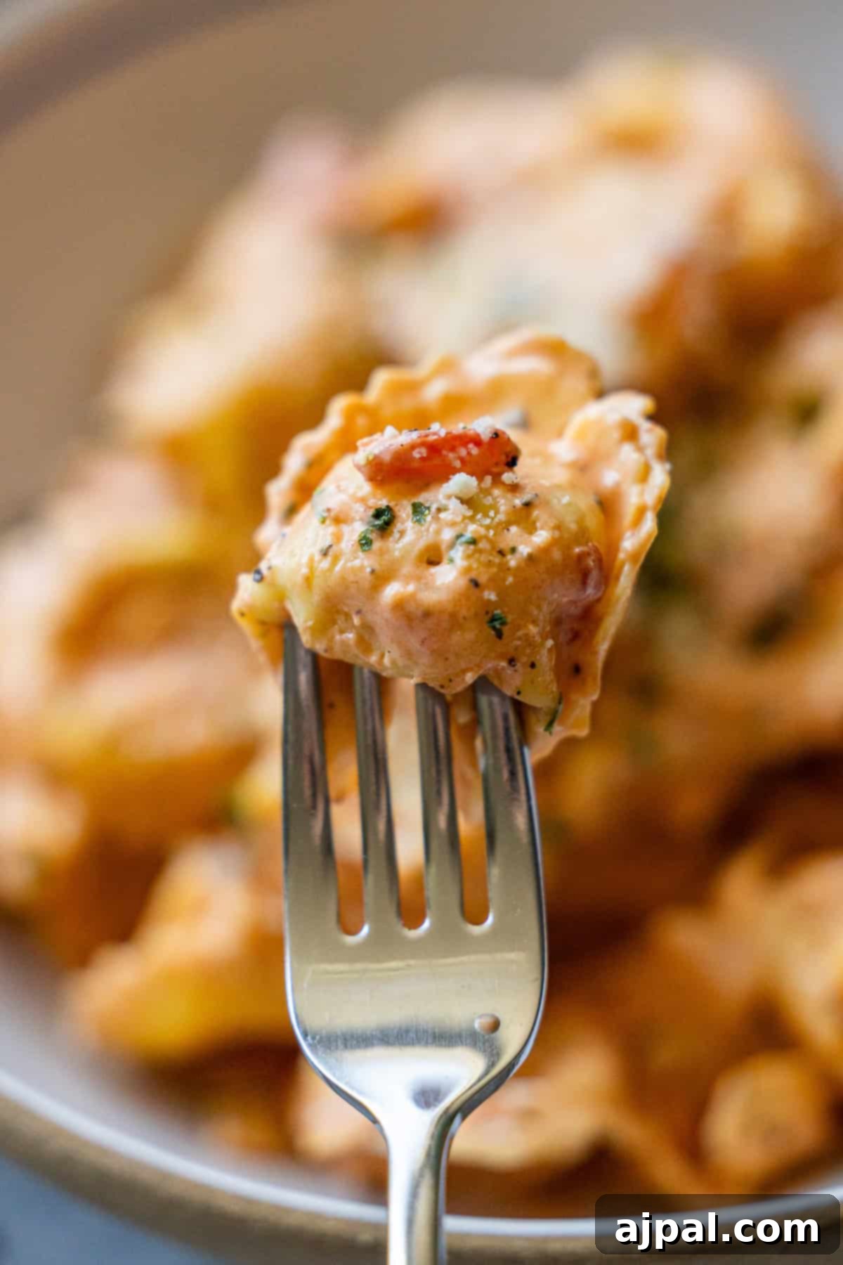 My Edible Soulmate: Tortellini 4 A close-up of a fork holding a piece of Marry Me Tortellini covered in creamy tomato sauce with herbs, with more tortellini in the blurred background.