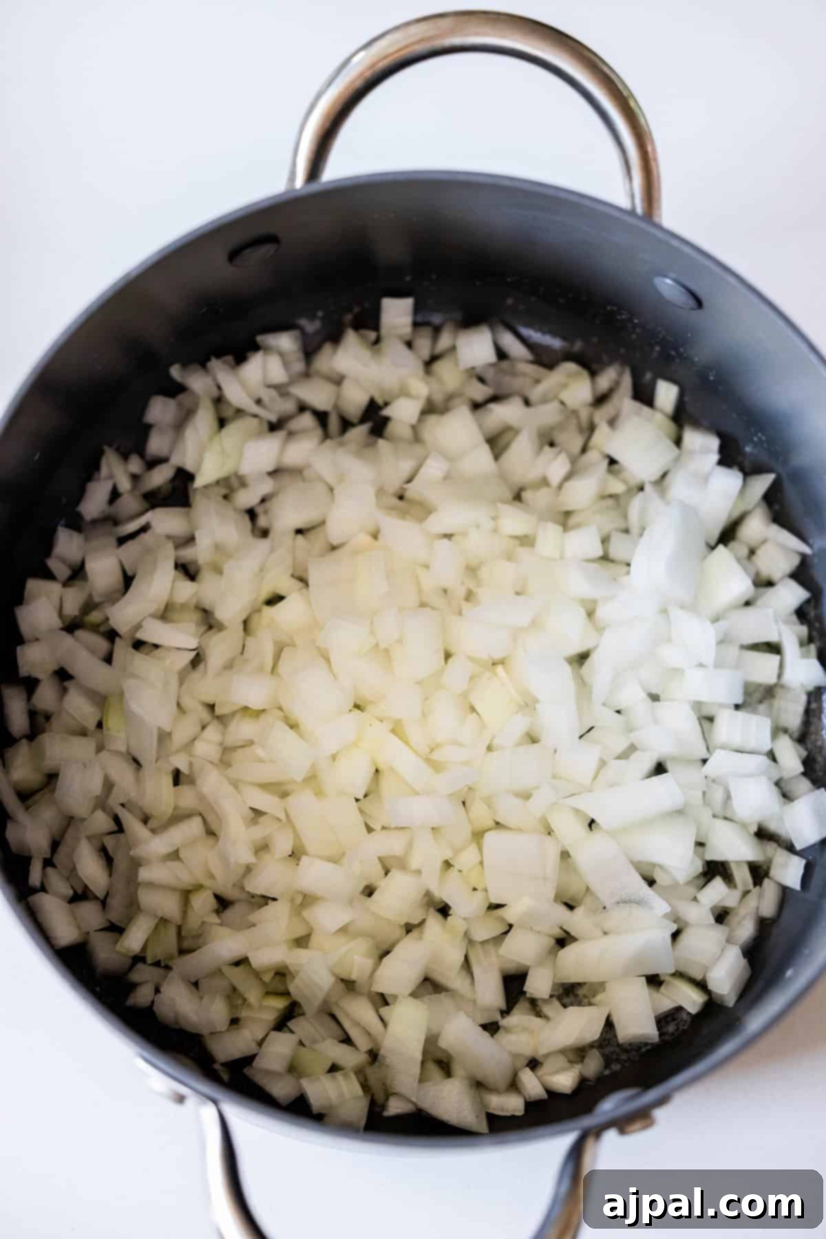 My Edible Soulmate: Tortellini 6 Chopped white onions in a black pot with metal handles, ready to be cooked for your favorite Marry Me Tortellini recipe.