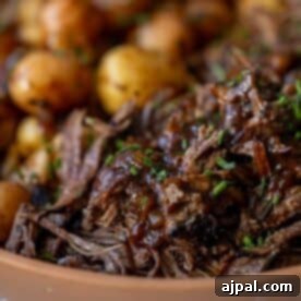 Close-up of Adobo Pot Roast shredded beef garnished with chopped chives, served next to roasted baby potatoes.