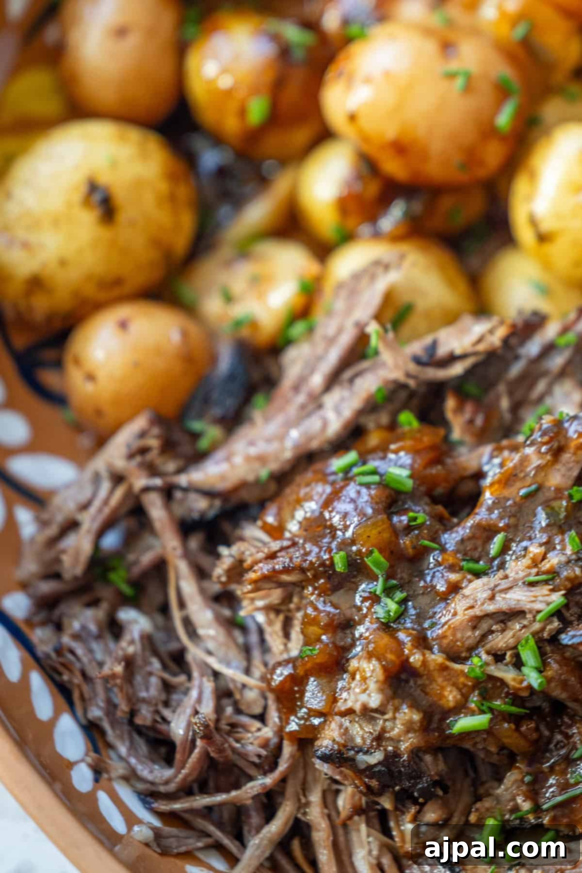 Shredded beef with sauce garnished with chopped chives, served alongside whole roasted baby potatoes.