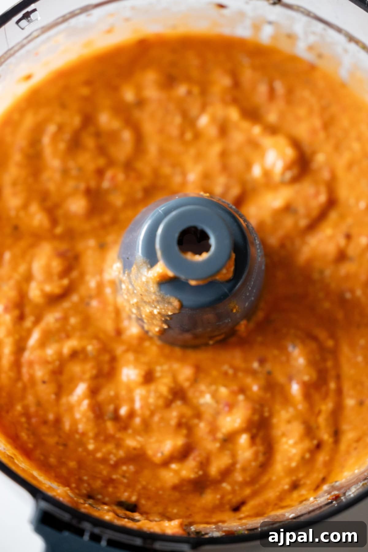 Red Pepper Feta White Bean Sensation 6 An overhead shot showcasing a thick, vibrant orange-red dip being blended to perfection in a food processor, creating a smooth and creamy texture.