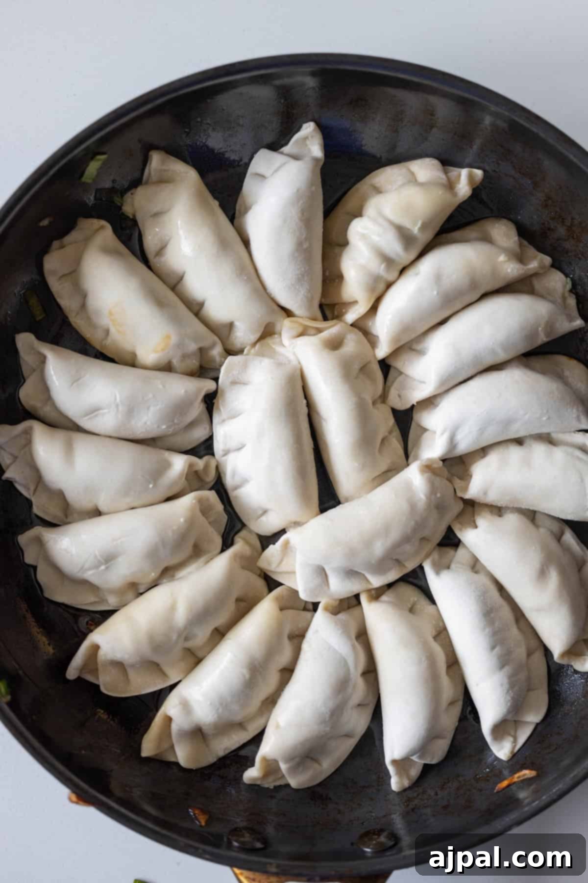 Spicy Potsticker Crunch Torte 6 A frying pan filled with uncooked dumplings, some with crisp Bok Choy tucked inside, arranged in a circular pattern and ready to be cooked into golden fried potstickers.