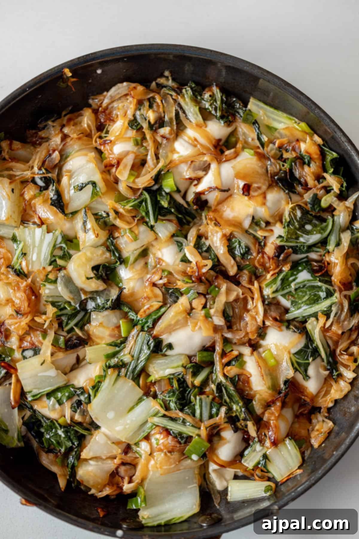 Spicy Potsticker Crunch Torte 7 A close-up of a pan filled with cooked bok choy, onions, and melted cheese, reminiscent of a savory fried potsticker, on a light background.