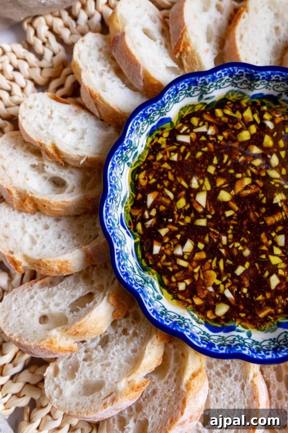A decorative bowl filled with chopped garlic and herbs in balsamic vinaigrette, surrounded by sliced pieces of crusty bread on a woven mat.
