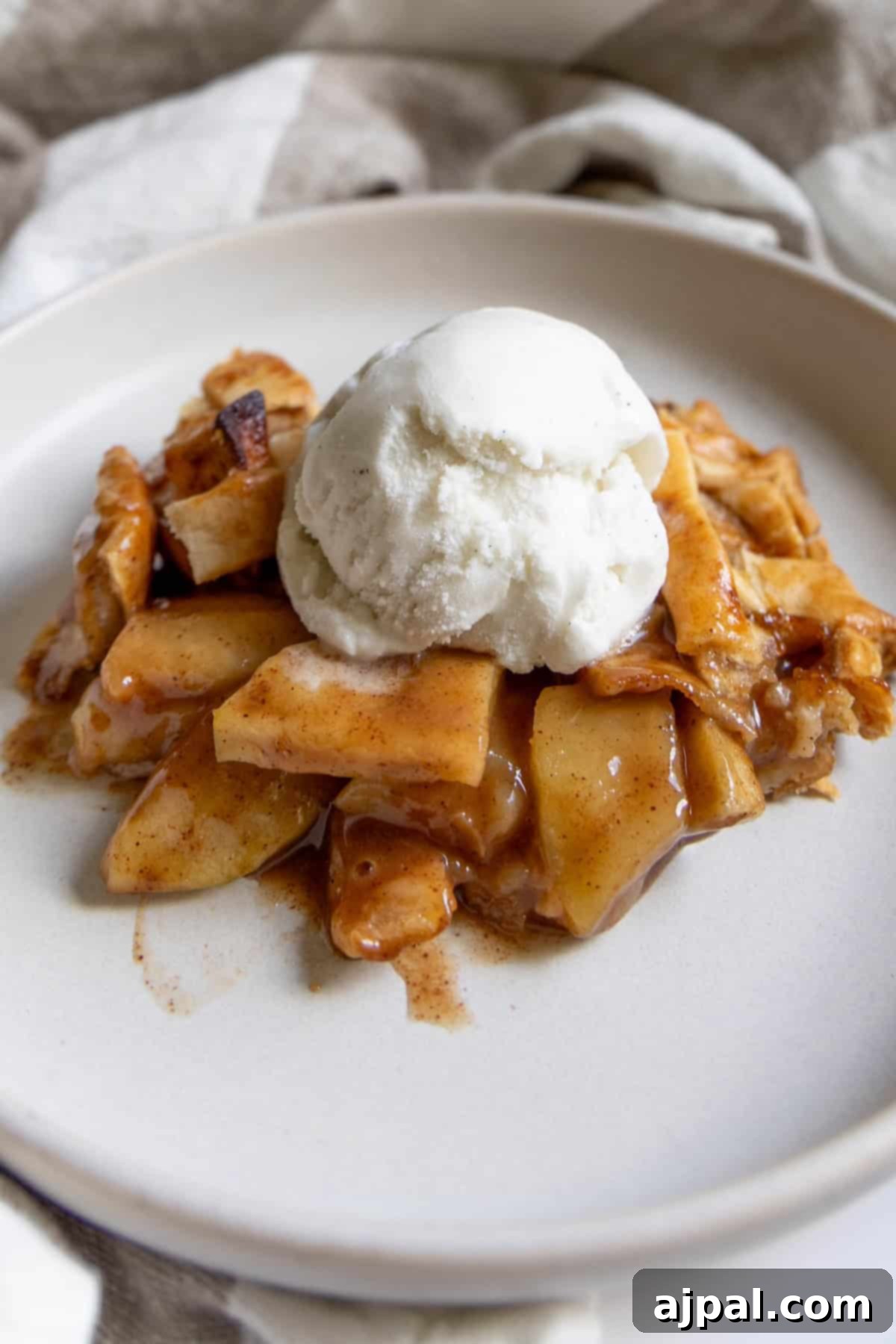 Heirloom Apple Pie 5 A delicious serving of apple pie topped with a scoop of vanilla ice cream sits on a white plate.