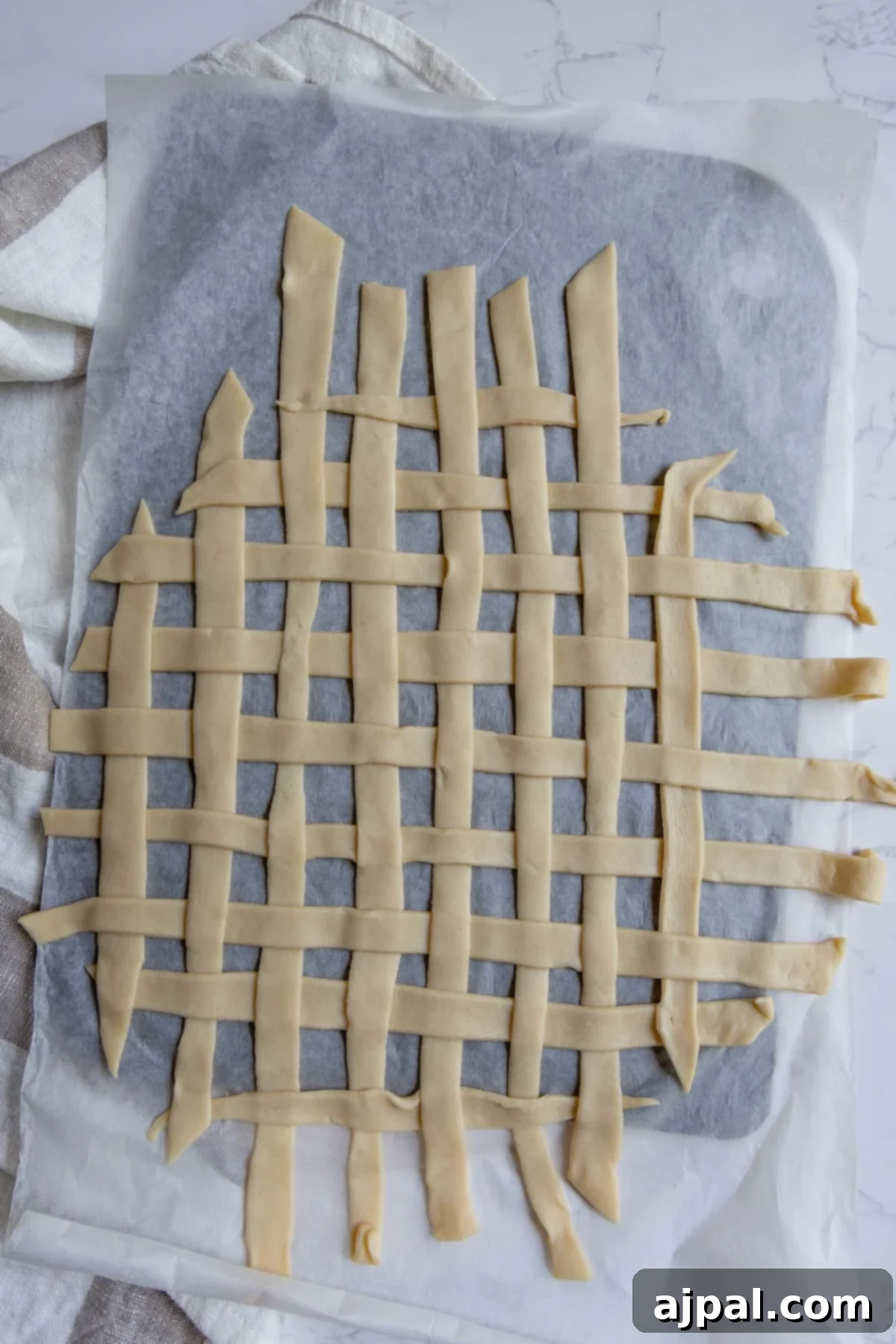 Heirloom Apple Pie 10 Unbaked lattice pie crust strips, perfect for an apple pie, are arranged in a grid pattern on parchment paper atop a baking sheet.