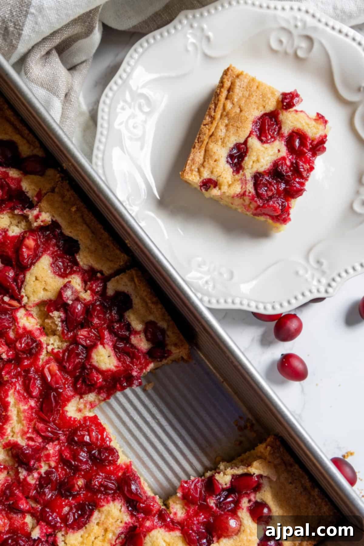 A neatly cut square of cranberry cake on a white plate, with the remaining bars in the baking pan, all ready to be enjoyed.
