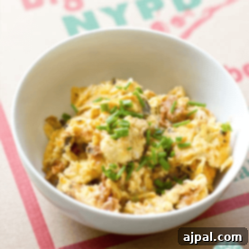 A white bowl filled with pizza eggs, garnished with chopped chives, placed on a cardboard surface.