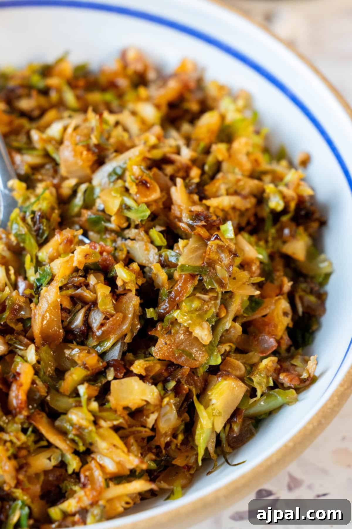A close-up of a bowl filled with sautéed, shredded vegetables, including Brussels sprouts, carrots, and onions, with a slightly crispy texture.