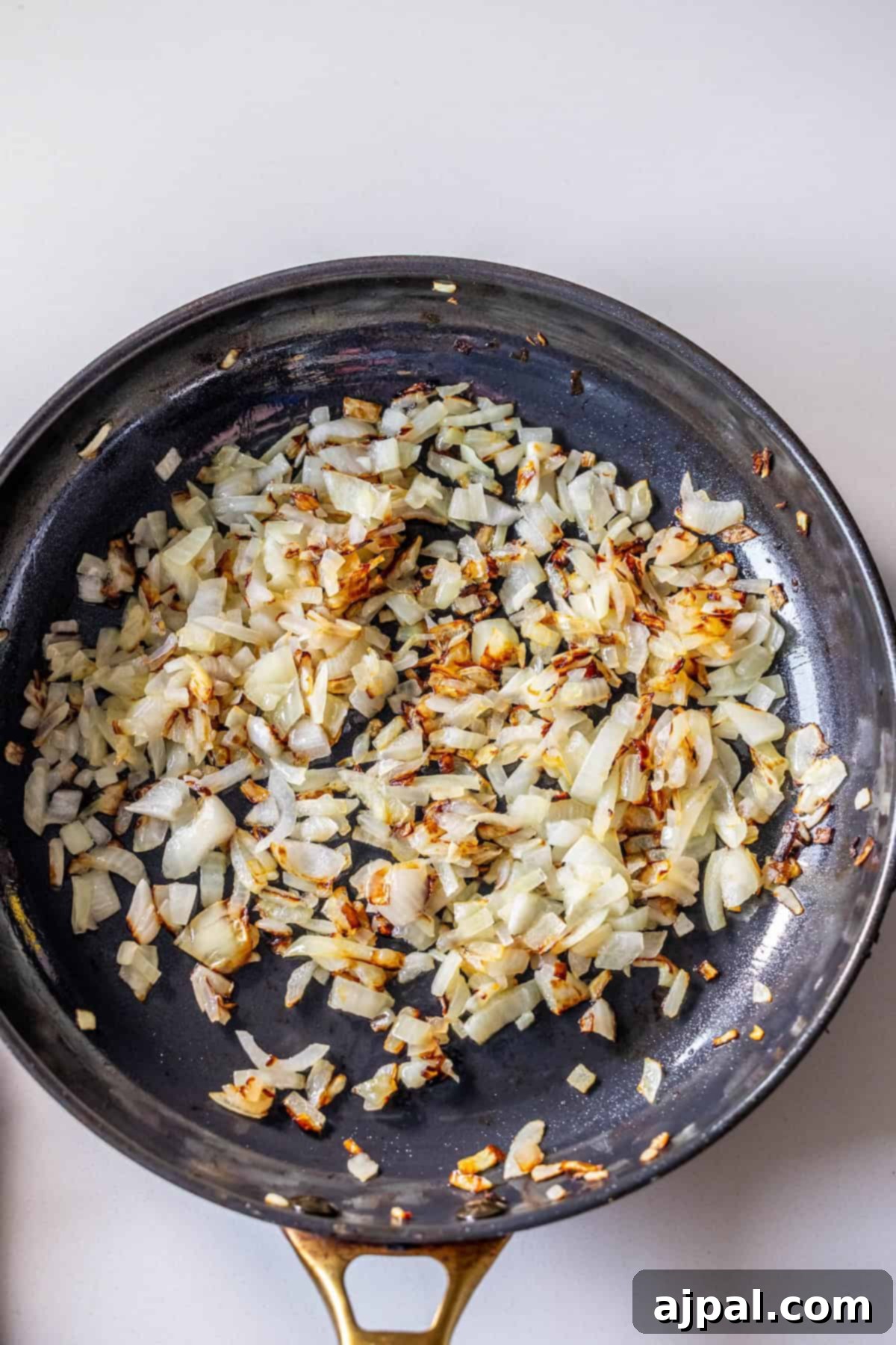 Chopped onions being sautéed in a black skillet with some pieces lightly browned, perfect as a savory base for a flavorful Brussels Sprouts Hash.