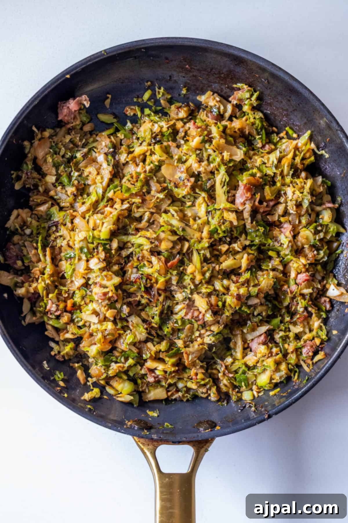 A skillet filled with savory Brussels Sprouts Hash, featuring cooked, shredded Brussels sprouts mixed with crispy pancetta and herbs, sits on a light background, ready to be served.